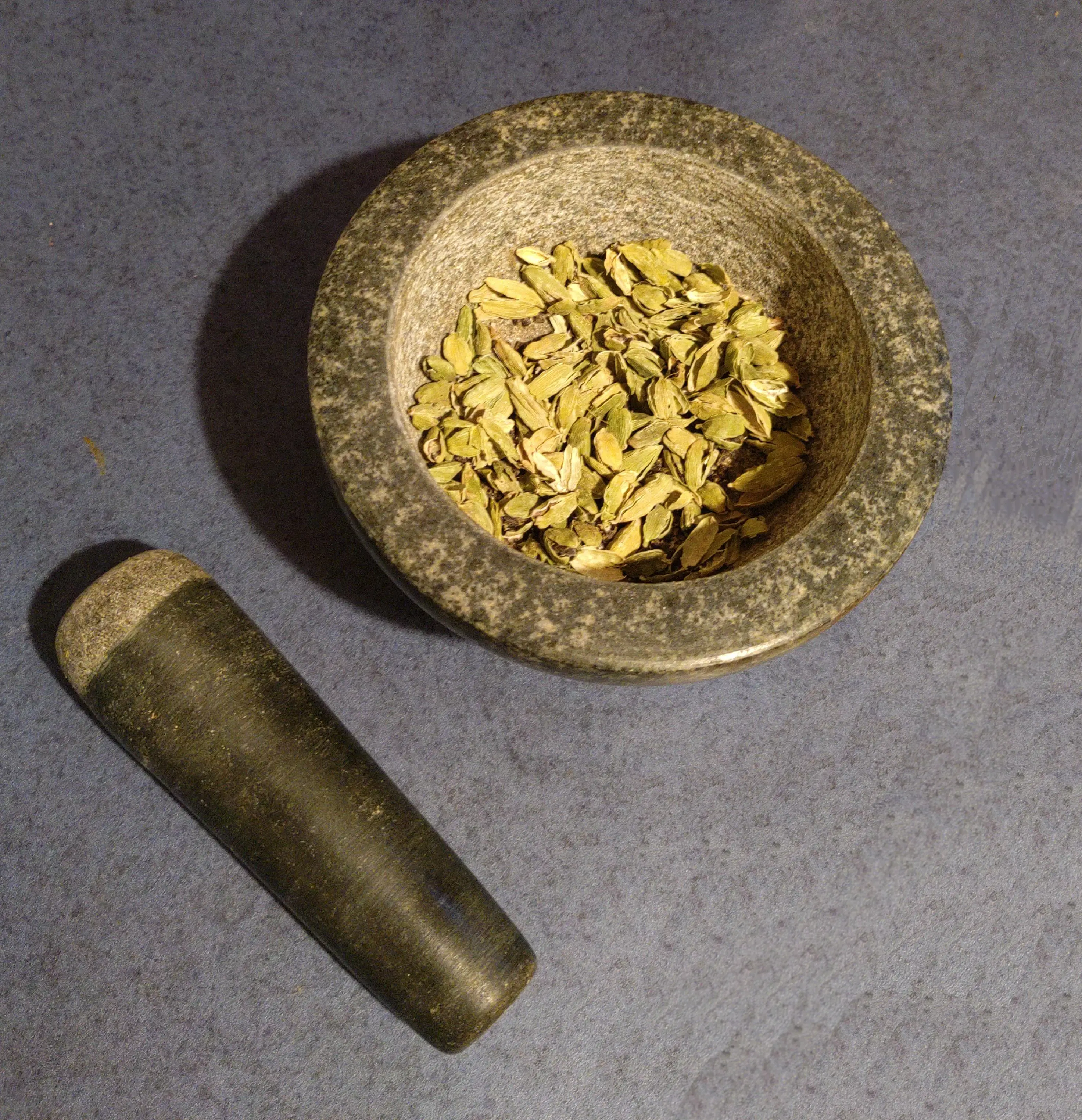 cardamon in a mortal with the pestle next to it