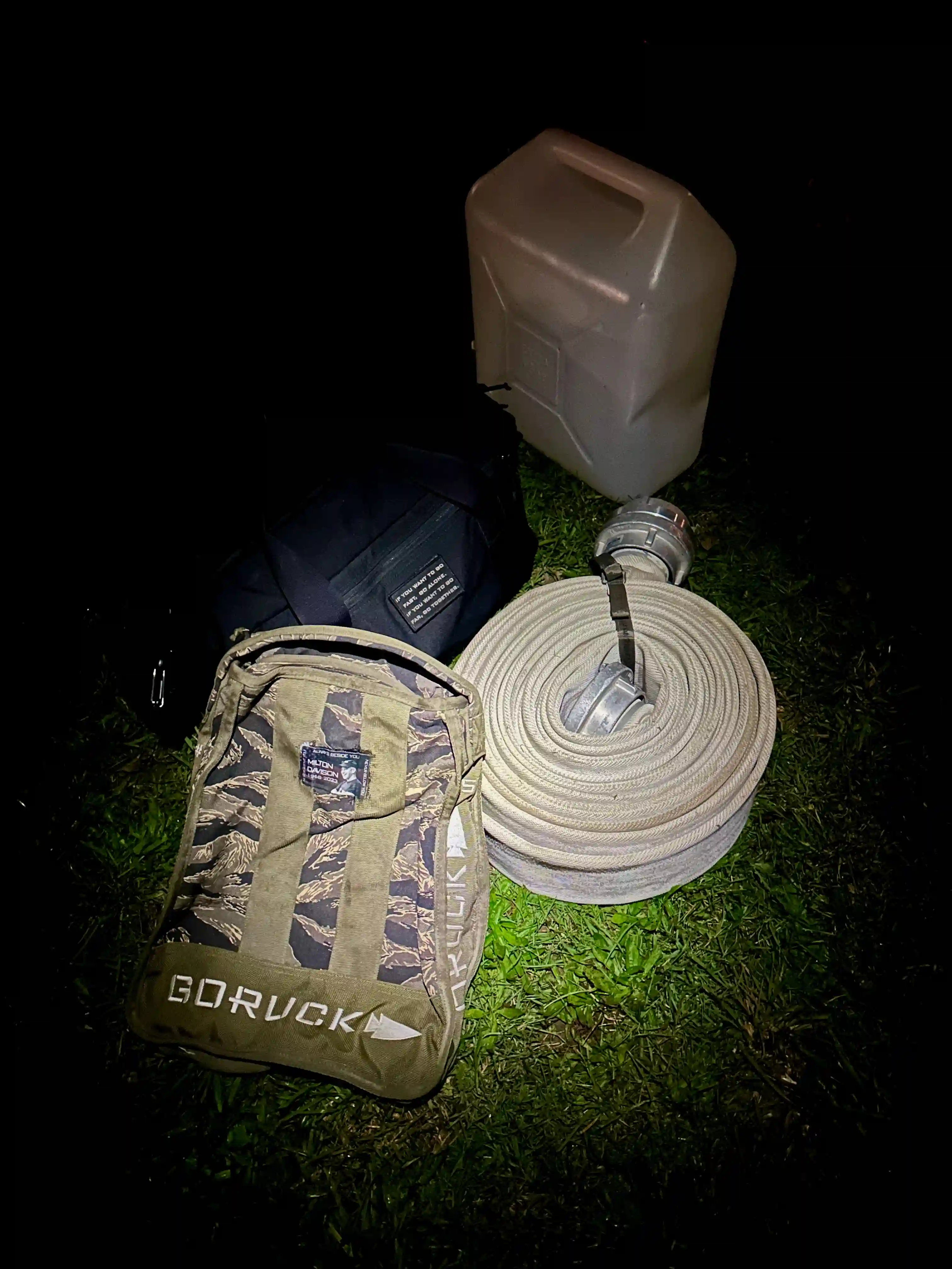 The coupons laid out with jerrycan filled with water, a rolled up fire hose, a bag filled with unknown goodies, and a sandbag jerrycan with the Milton Memorial patch glued onto it